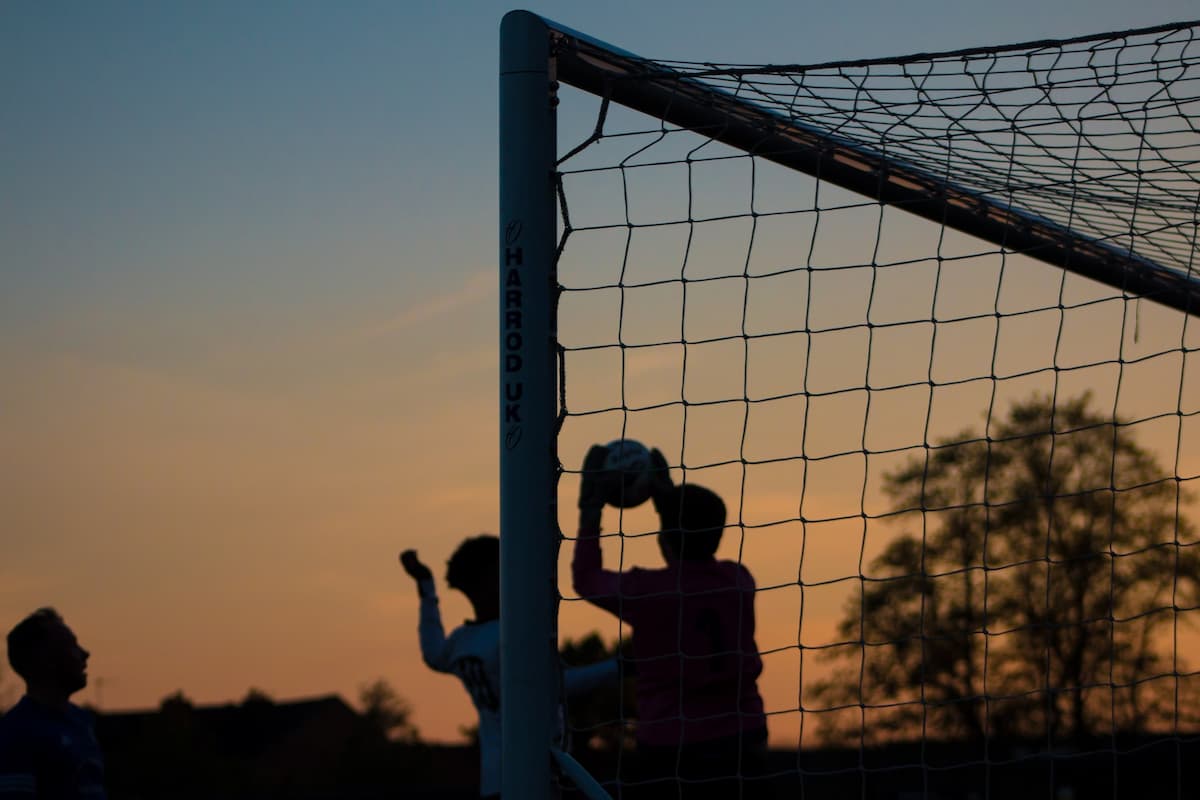 A goalkeeper making a high claim in front of the goalpost.